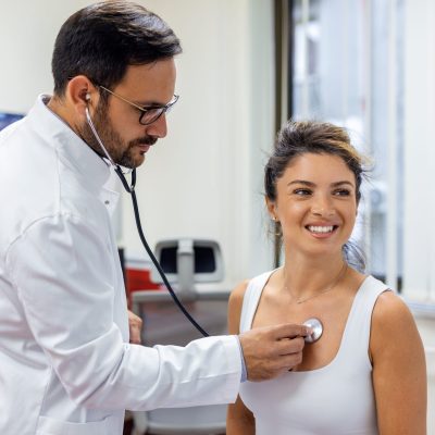 Young doctor listen to female patient heart chest with stethoscope at clinic meeting. Man GP checkup examine woman client with phonendoscope. healthcare concept.