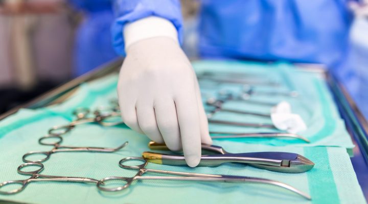 Surgeon picking up surgical tool from tray. Surgeon is preparing for surgery in operating room. He is in a hospital.